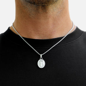Silver necklace with a pendant worn by a person on a plain background