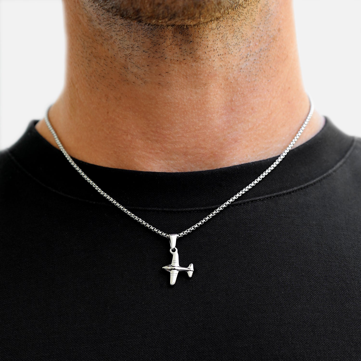 Person wearing a necklace with an airplane pendant on a plain background