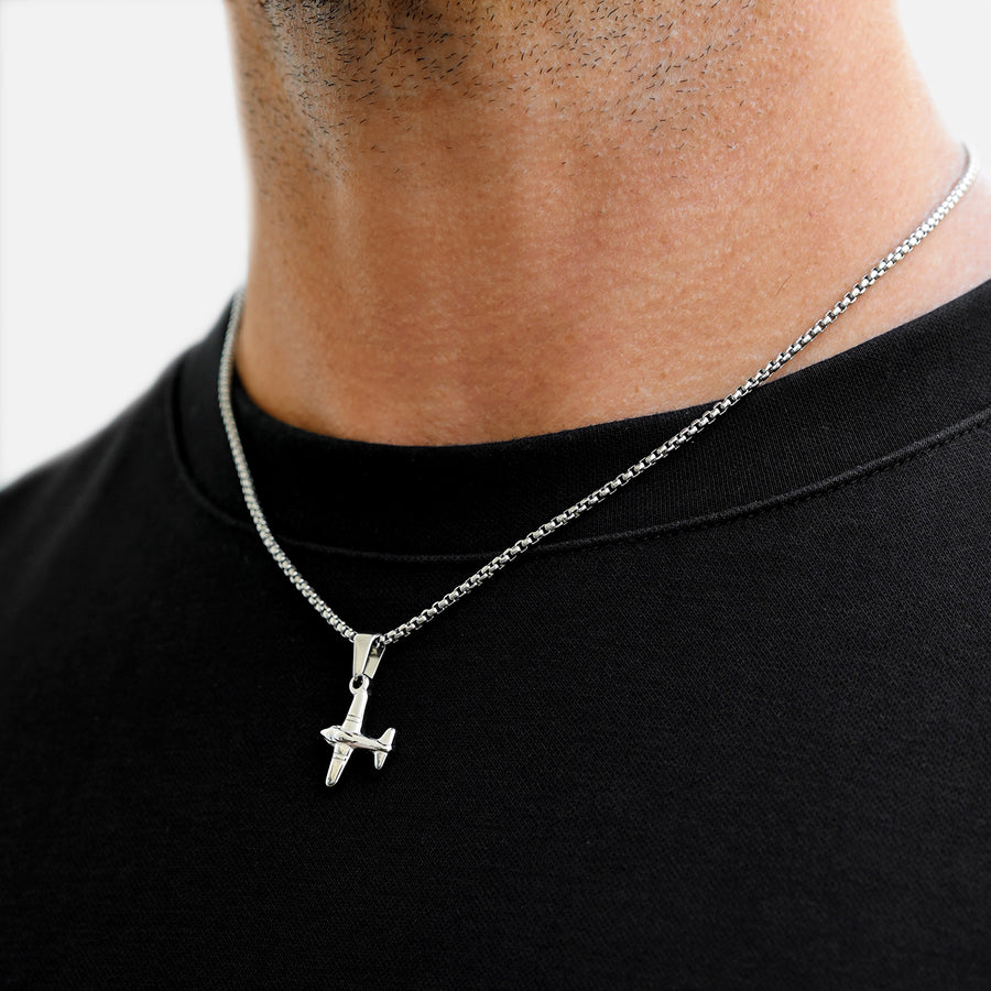 Silver necklace with a pendant worn by a person on a black shirt against a white background