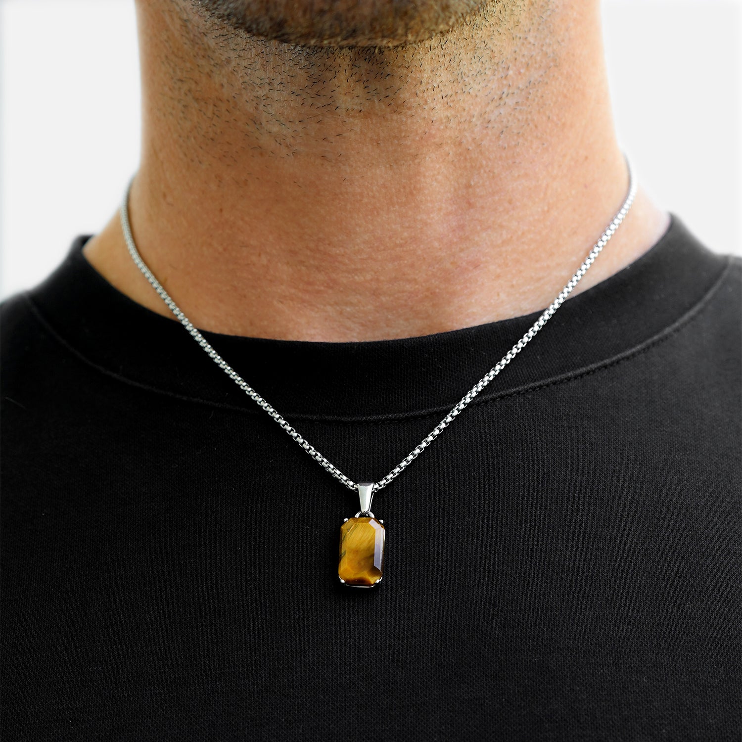 Person wearing a silver necklace with a tiger's eye pendant on a plain background