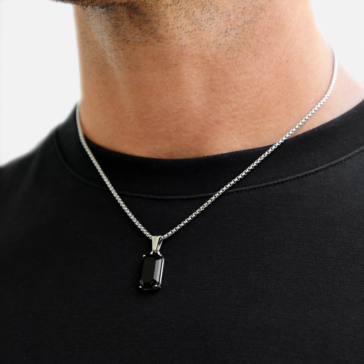 Person wearing a black pendant necklace on a plain background