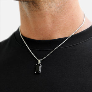 Person wearing a black pendant necklace on a plain background