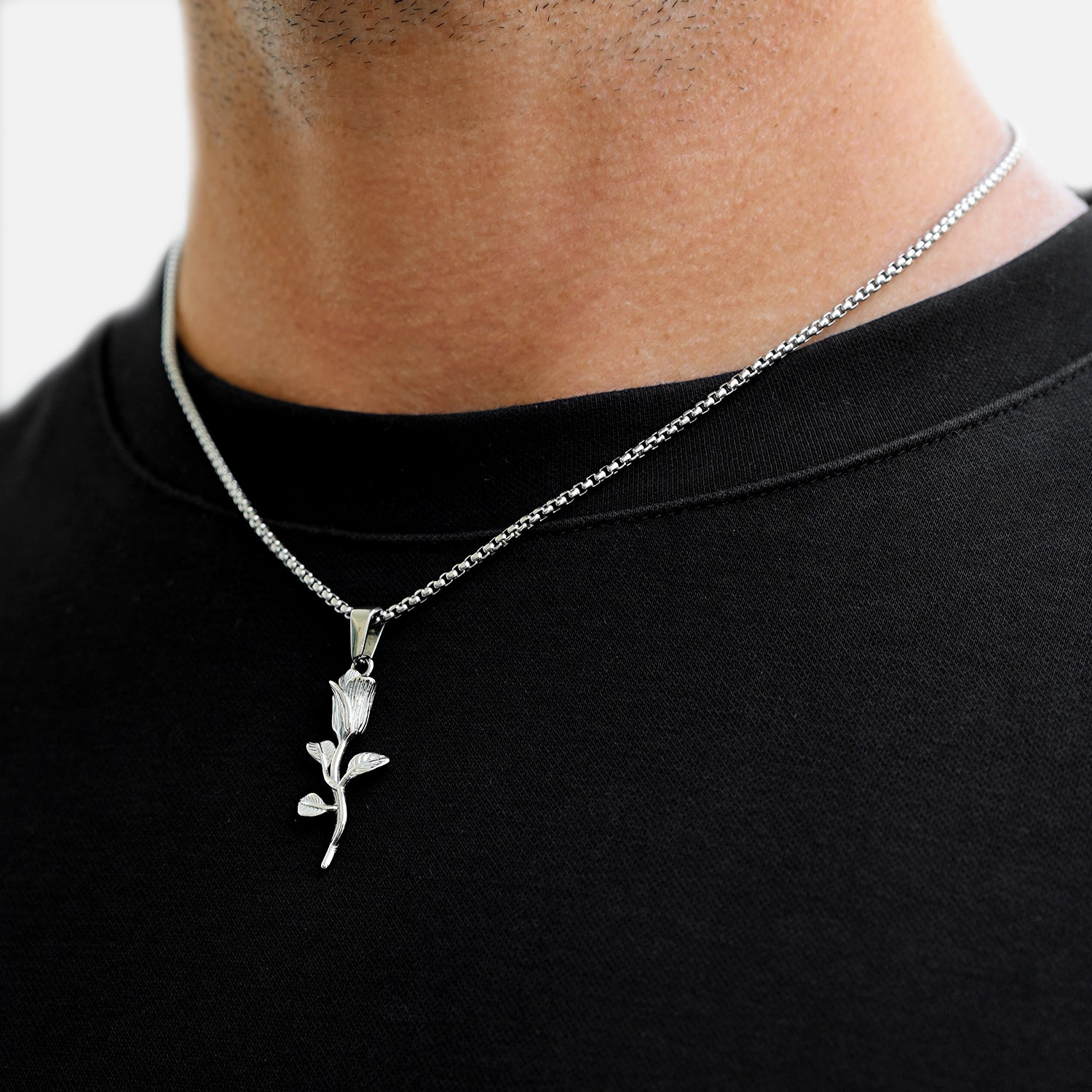 Silver necklace with a leaf pendant worn by a person on a black shirt.
