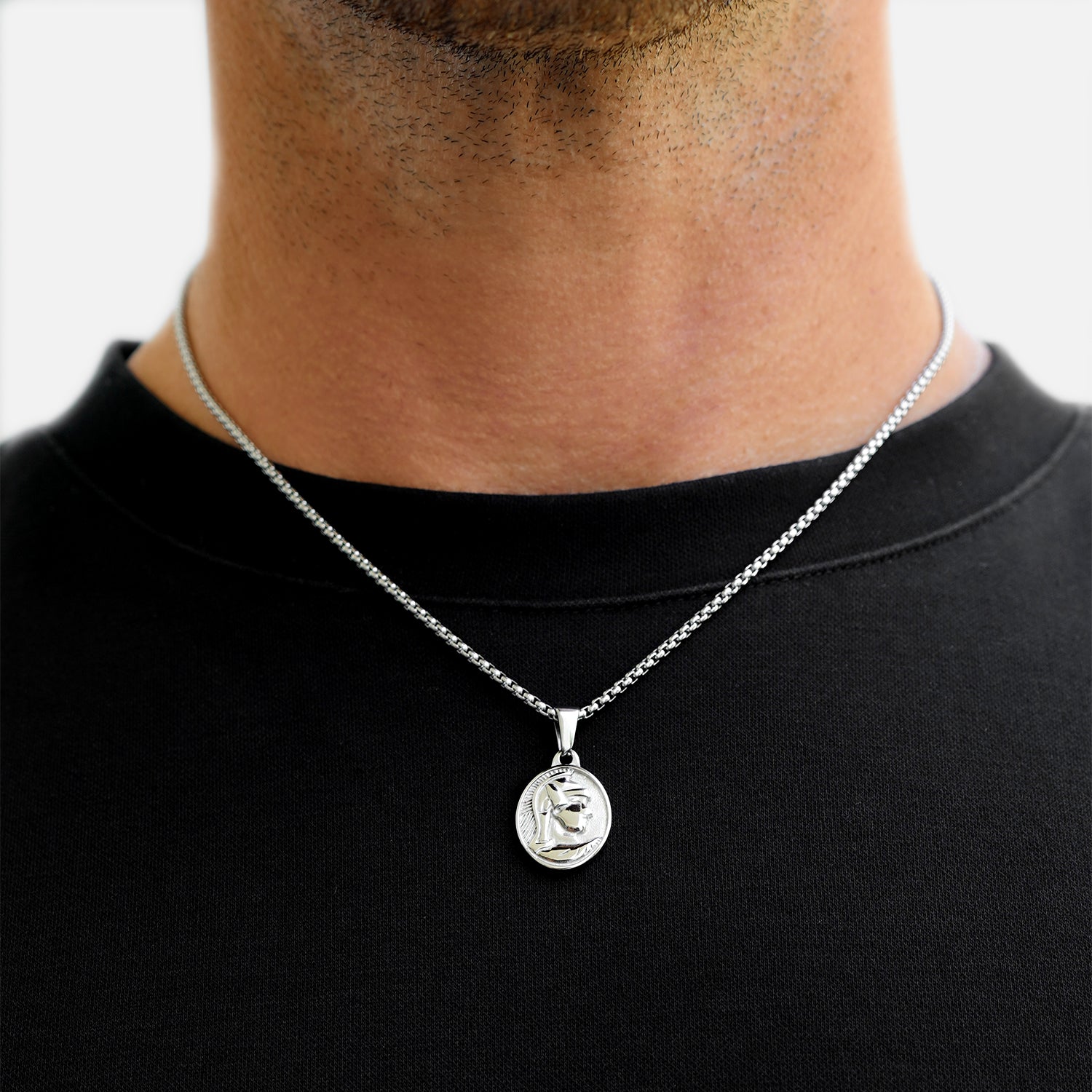 Silver necklace with a pendant on a person wearing a black shirt against a white background