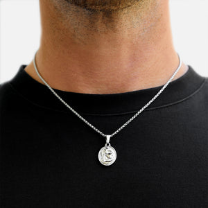Silver necklace with a pendant on a person wearing a black shirt against a white background