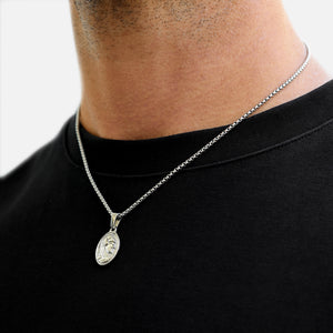 Silver necklace with a pendant on a person wearing a black shirt.