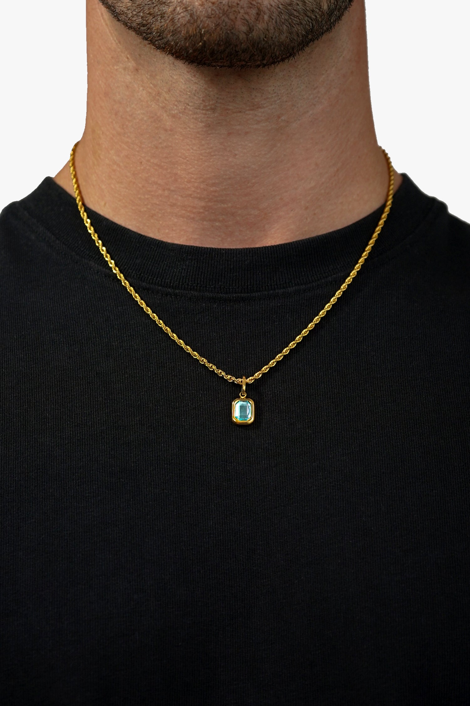 FRNE glacier blue gemstone gold necklace worn by a person, featuring a small rectangular light blue stone pendant set in gold on a rope-style gold chain, displayed against a black shirt for contrast