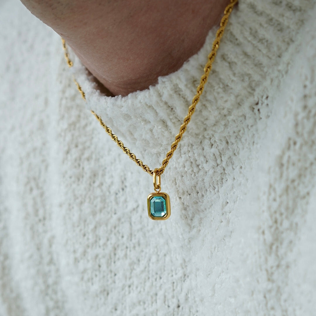 FRNE glacier blue gemstone gold pendant necklace worn by a person, featuring a rectangular light blue stone set in a gold frame on a twisted gold chain styled with a textured white sweater