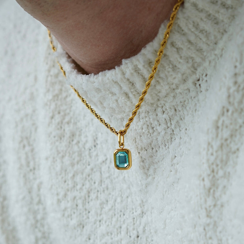 FRNE glacier blue gemstone gold pendant necklace worn by a person, featuring a rectangular light blue stone set in a gold frame on a twisted gold chain styled with a textured white sweater