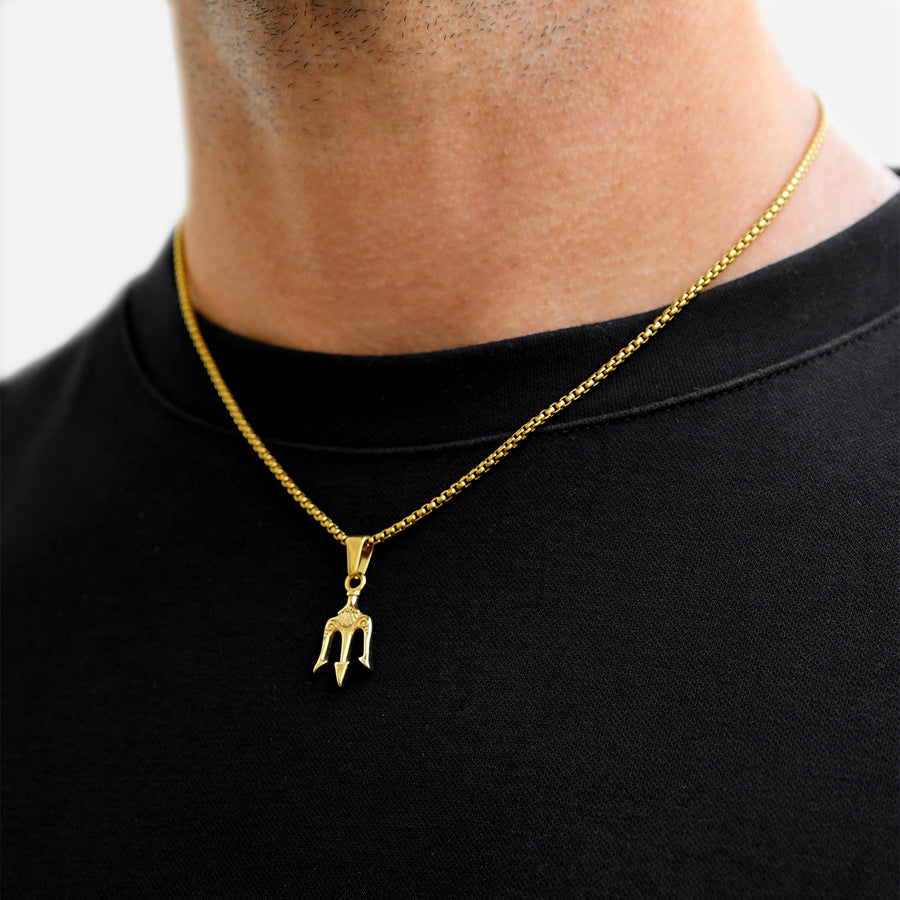 Close-up of a gold trident pendant necklace worn on a gold chain against a black shirt