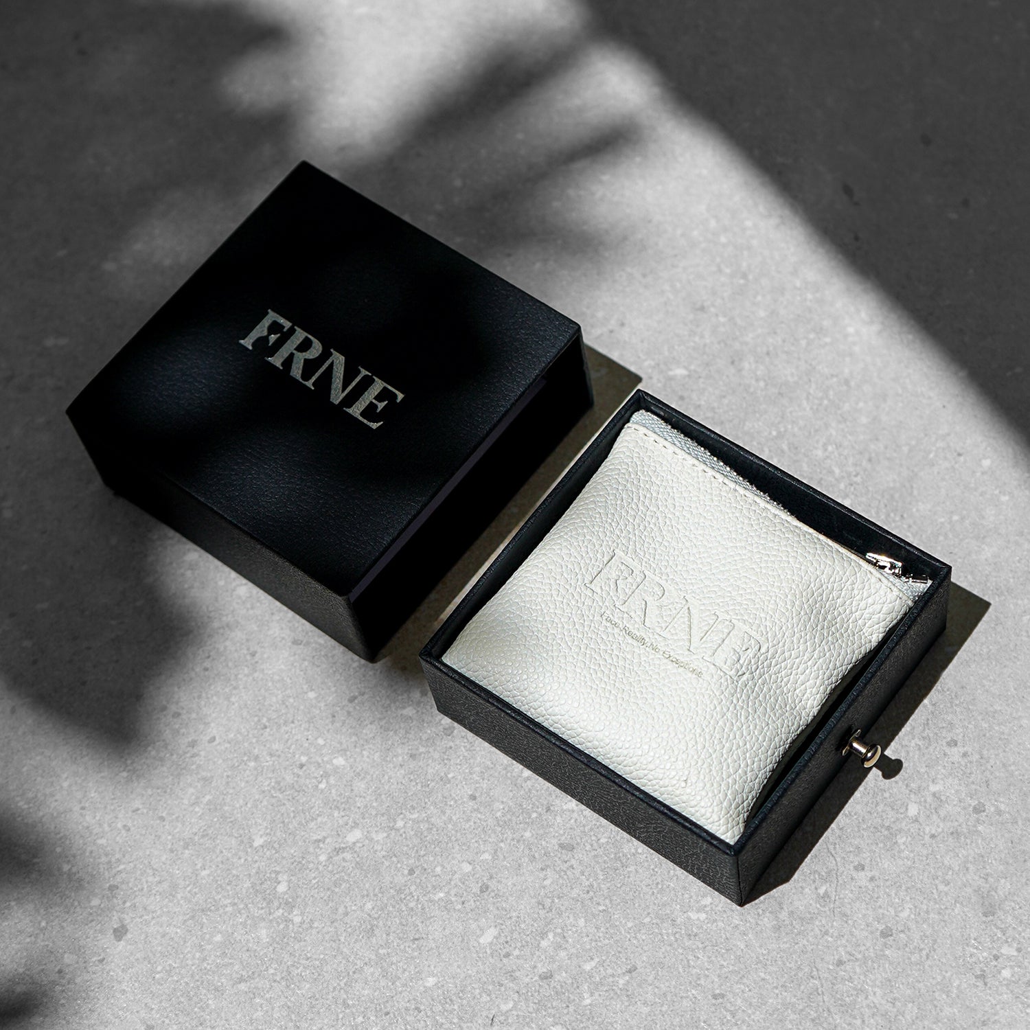 FRNE branded black jewellery box with a white pouch inside placed on a textured surface in natural light