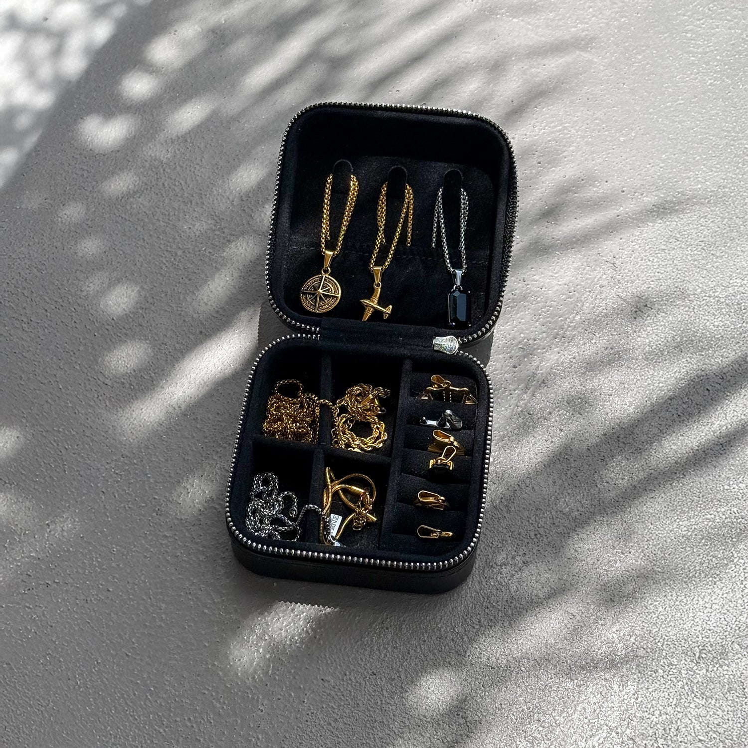 Open black jewellery travel case displaying gold and silver necklaces, rings, and accessories neatly organised on a textured surface