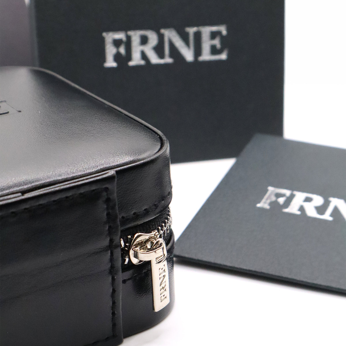 Close-up of a black leather jewellery case with a branded zipper pull and FRNE packaging in the background