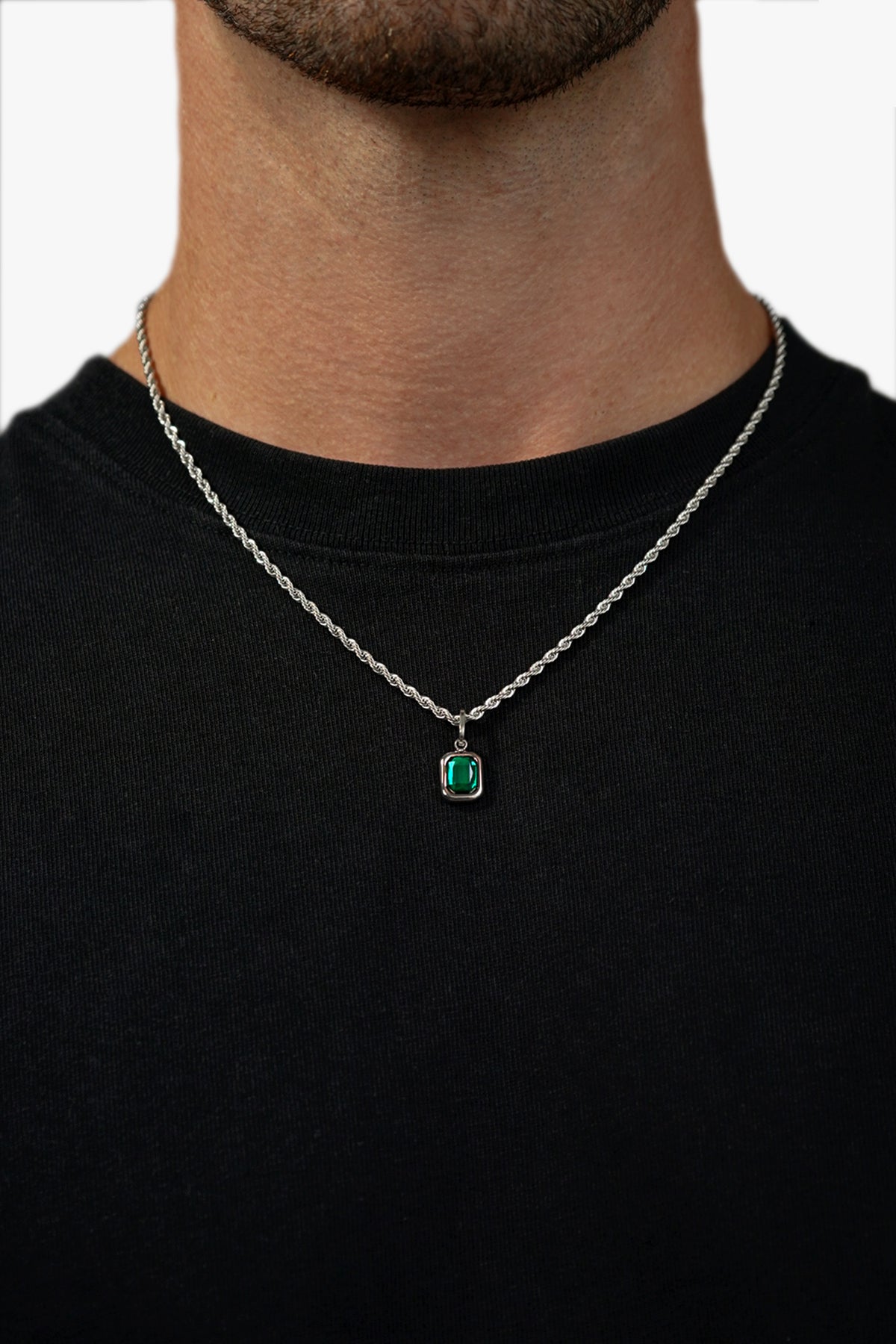 Person wearing a silver chain necklace with a rectangular green gemstone pendant against a black shirt
