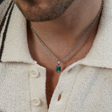 Person wearing a silver chain necklace with a rectangular green gemstone pendant, styled with a cream knit sweater