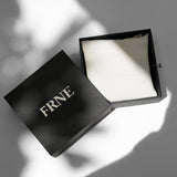 Open FRNE black jewellery box with a white pouch inside displayed on a clean surface with soft natural shadows