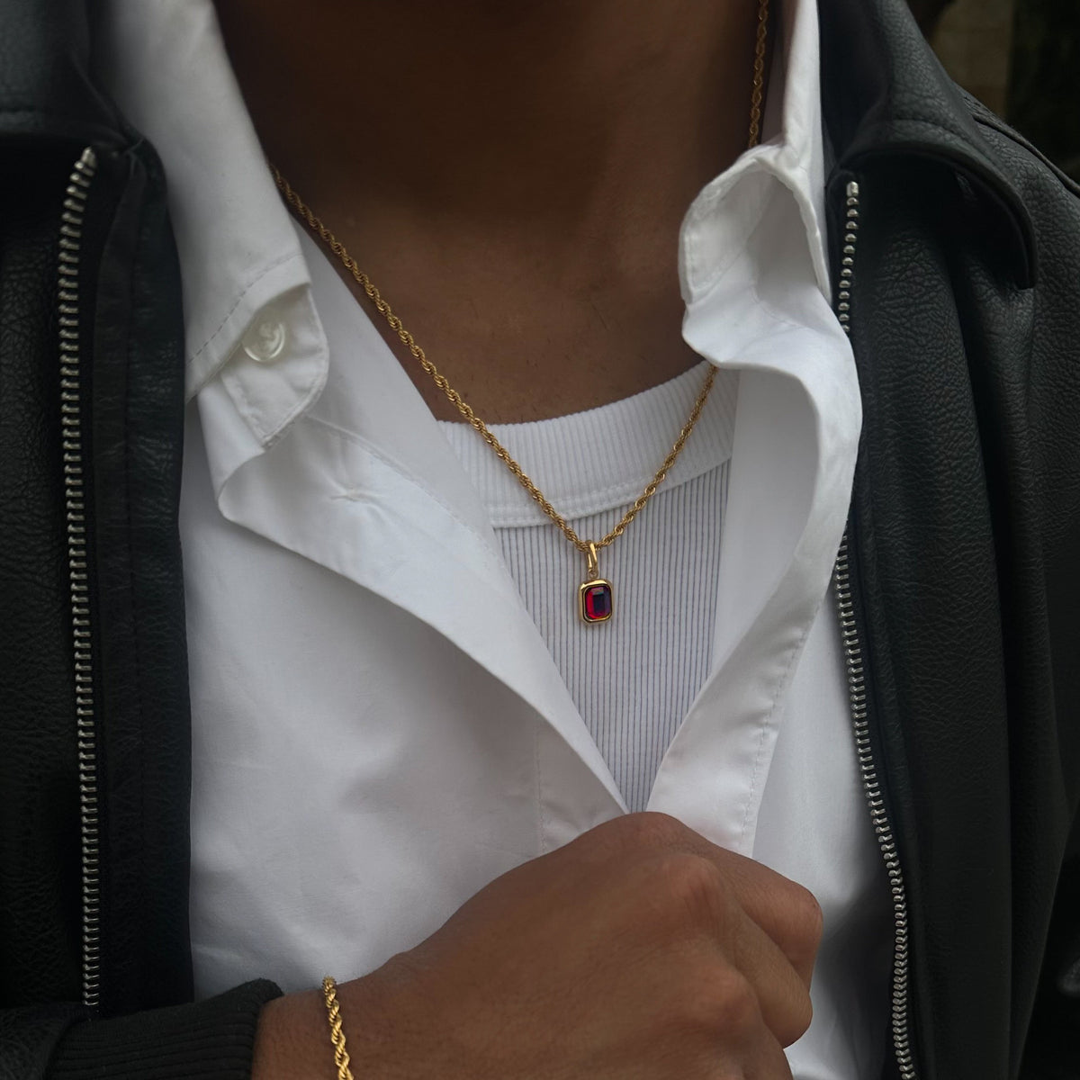 FRNE ruby centre red gemstone gold necklace worn by a person, featuring a rectangular deep red stone pendant on a gold chain, styled with a white shirt and black leather jacket, with a gold bracelet visible