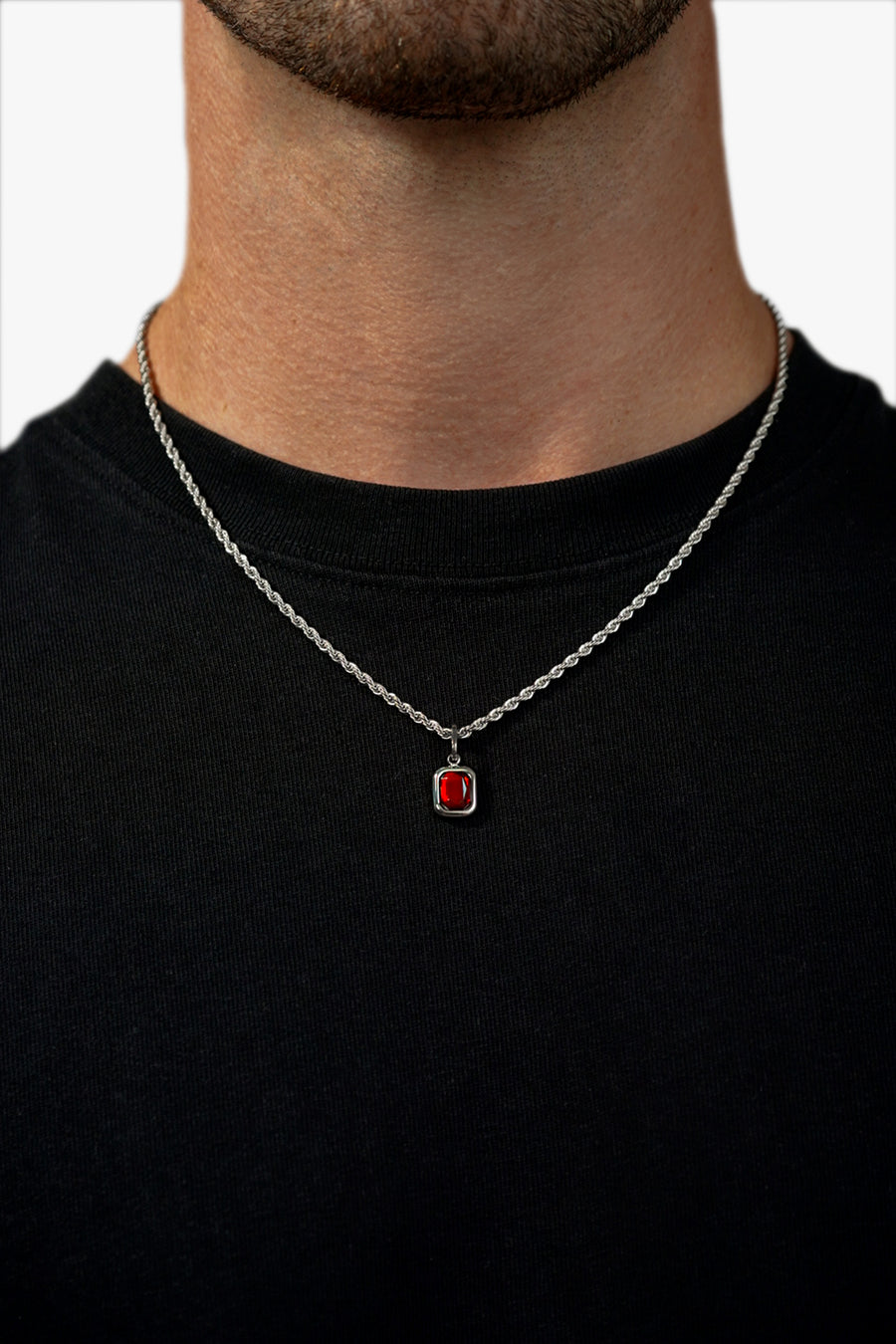 FRNE ruby flame red gemstone silver necklace worn by a person, featuring a small rectangular deep red stone pendant set in silver on a rope-style chain, styled against a black shirt for contrast
