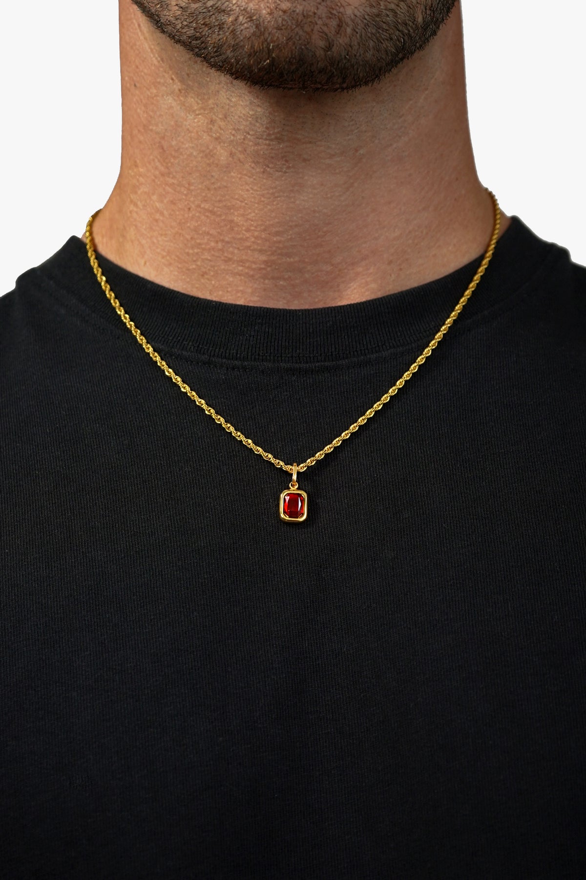 FRNE ruby flame red gemstone gold necklace worn by a person, featuring a rectangular deep red pendant on a gold chain, styled against a black shirt for contrast