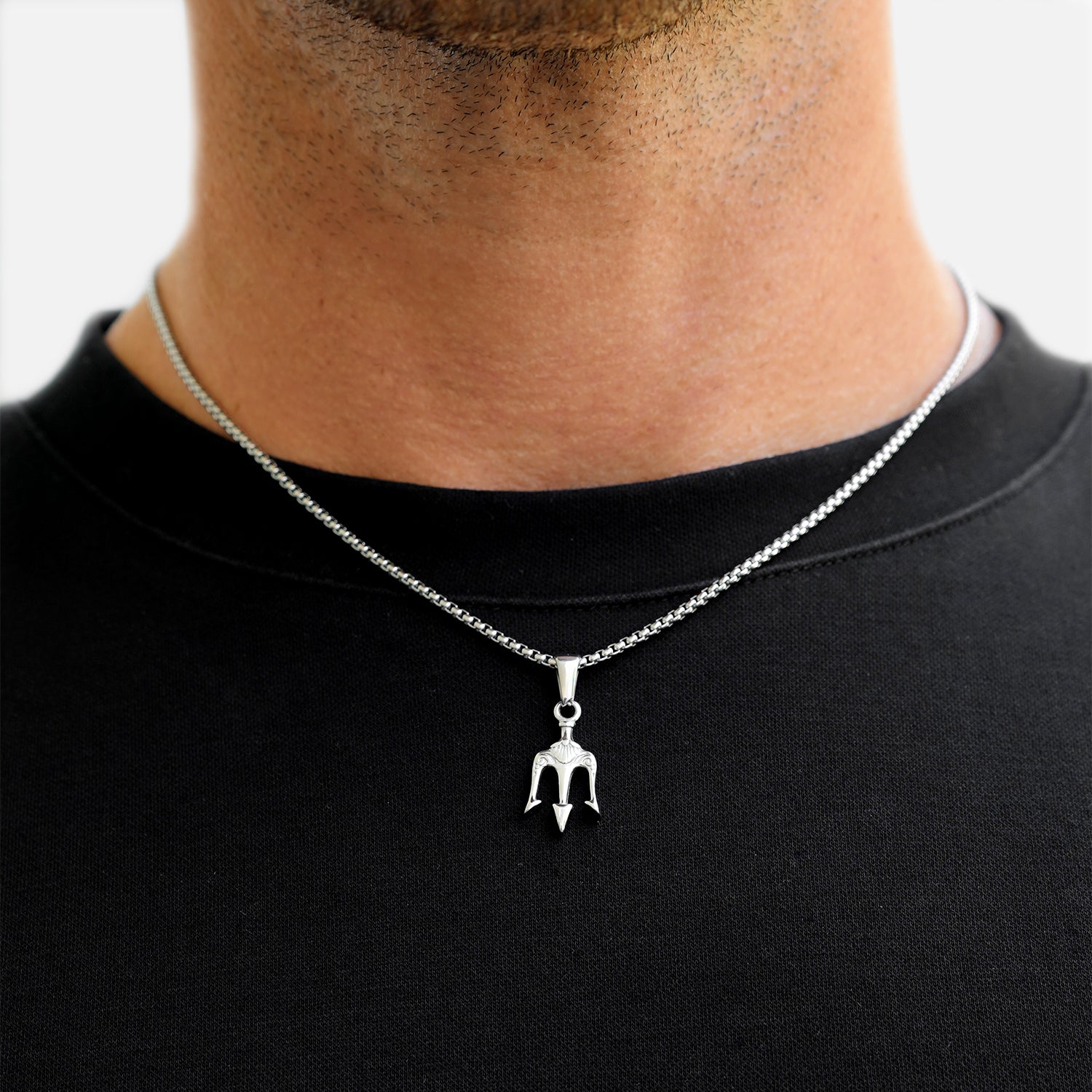 Silver trident pendant necklace worn by a person on a black shirt against a white background