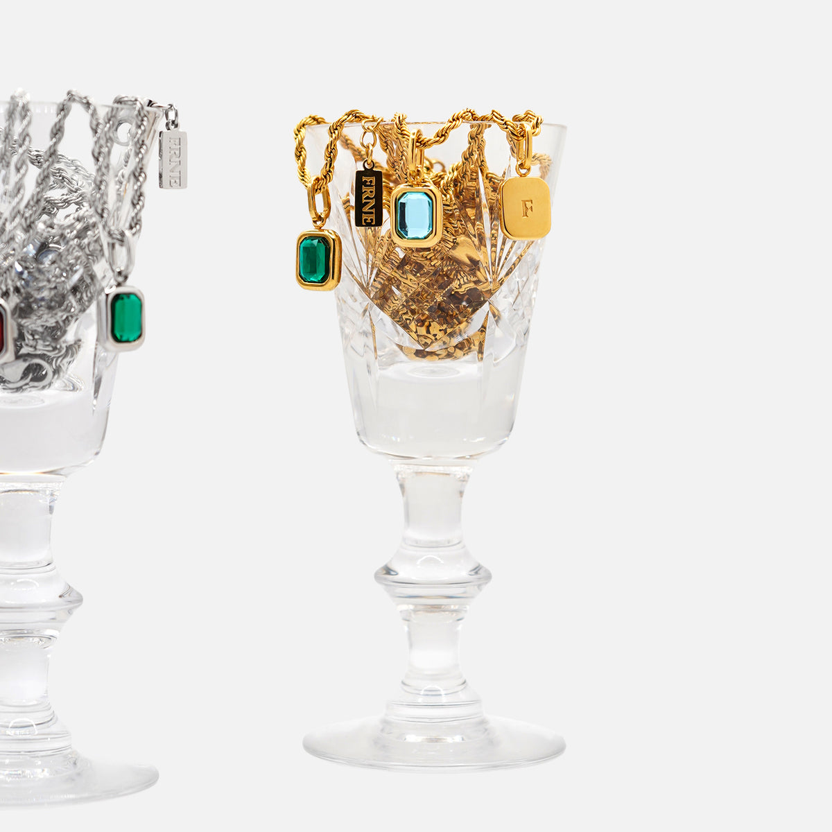 Gold pendant necklaces with rectangular gemstone charms displayed in glass cup on white background
