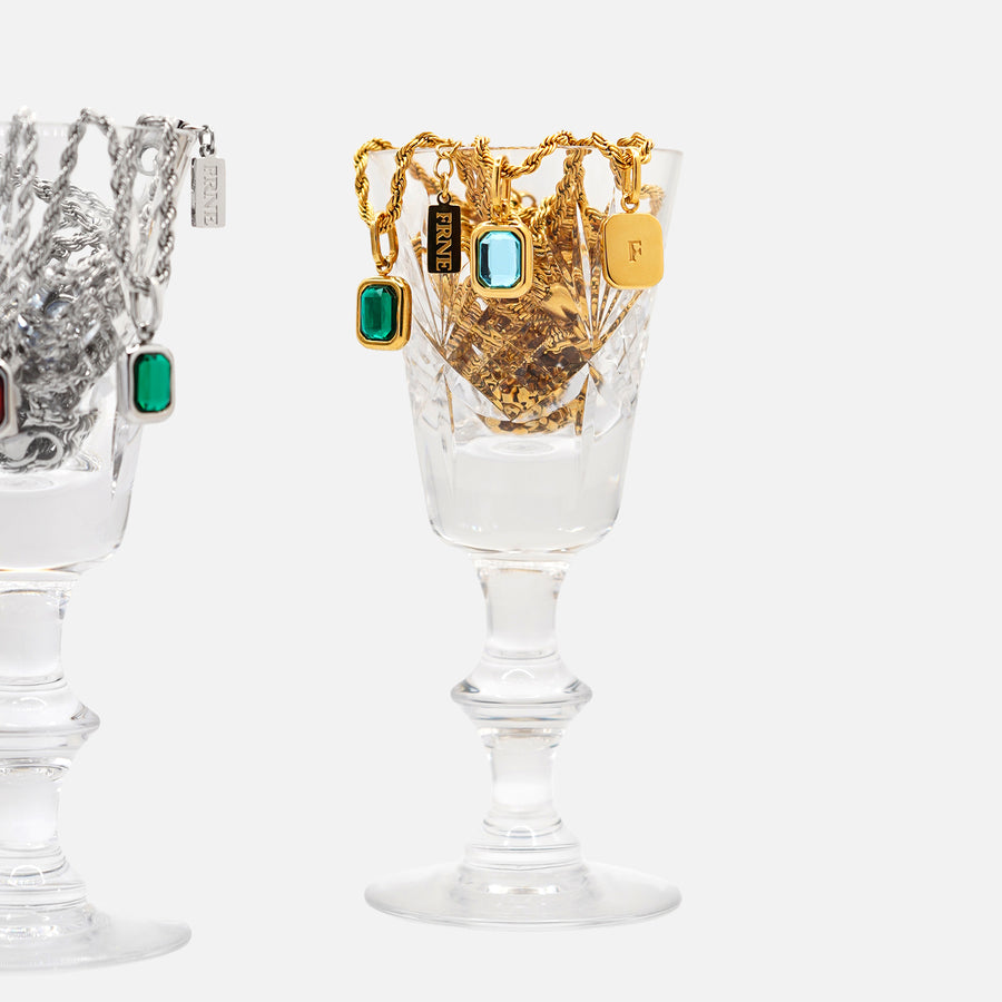 Gold pendant necklaces with rectangular gemstone charms displayed in glass cup on white background