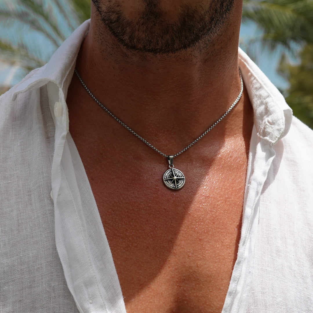 Man wearing a white shirt with a necklace featuring a compass pendant.