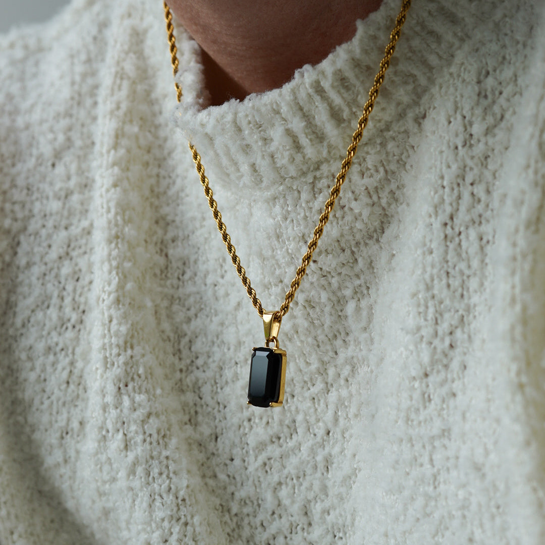 Gold necklace with a black pendant worn by a person in a white sweater.