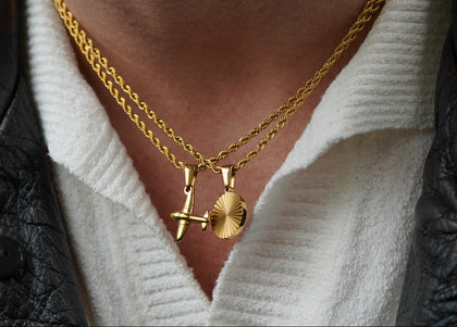 Close-up of a person wearing gold necklaces with airplane and sun pendants.