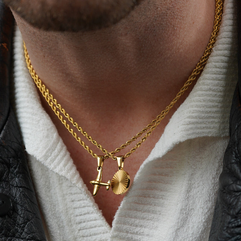 Close-up of a person wearing gold necklaces with airplane and sun pendants.
